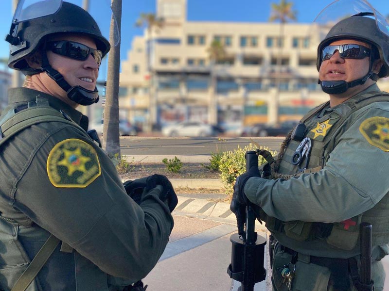 Two Sheriff Deputies wearing helmets and tactical gear outdoors in an urban area, possibly during a patrol or demonstration.